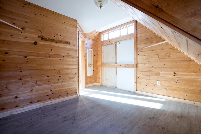 additional living space featuring wood walls, light wood-type flooring, and vaulted ceiling