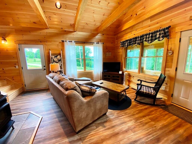 living room with wood walls, light hardwood / wood-style floors, vaulted ceiling with beams, a wood stove, and wood ceiling