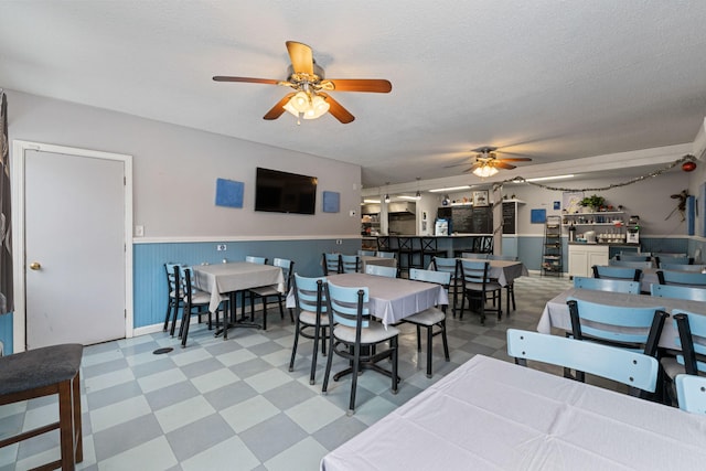 dining space with tile patterned floors, wainscoting, ceiling fan, and a textured ceiling