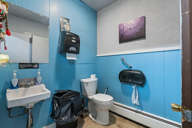 half bath with wainscoting, toilet, a baseboard heating unit, and a sink