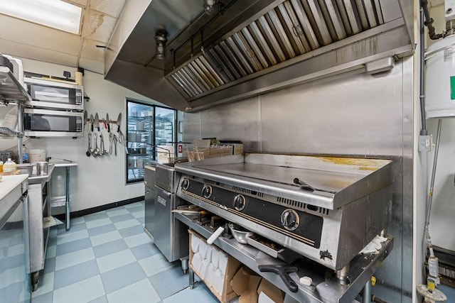 kitchen featuring baseboards, stainless steel microwave, a drop ceiling, and light floors