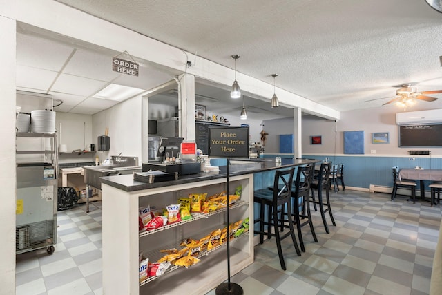 kitchen with light floors, baseboard heating, dark countertops, ceiling fan, and a drop ceiling