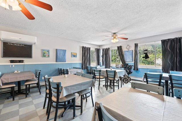 dining area featuring a wainscoted wall, tile patterned floors, a ceiling fan, a wall unit AC, and a textured ceiling