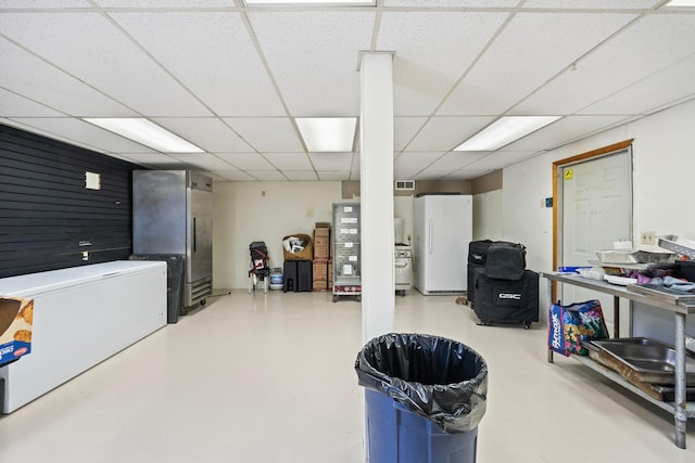 basement with visible vents, a paneled ceiling, and freestanding refrigerator