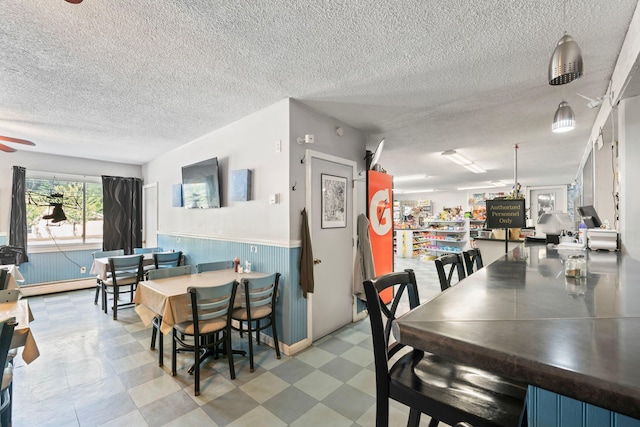 dining area featuring a textured ceiling, tile patterned floors, a wainscoted wall, a ceiling fan, and baseboard heating