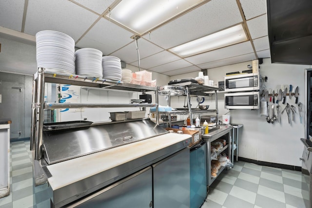 kitchen featuring baseboards, a drop ceiling, light floors, and stainless steel microwave