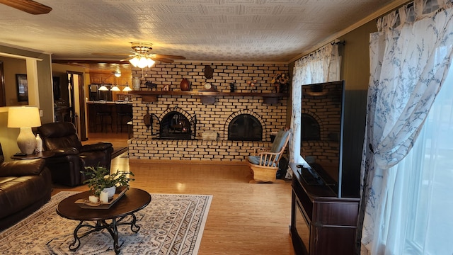 living room featuring ceiling fan, light hardwood / wood-style floors, a brick fireplace, brick wall, and ornamental molding