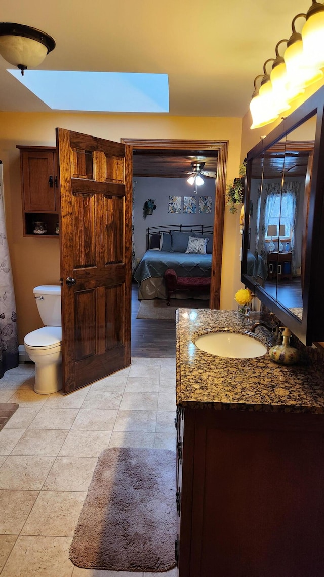 bathroom featuring tile flooring, ceiling fan, toilet, vanity, and a skylight