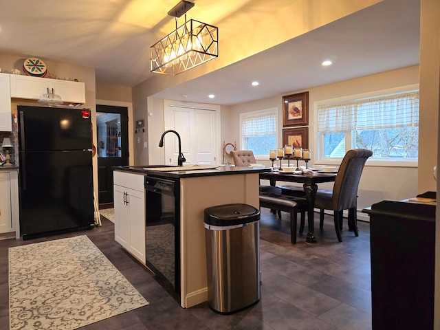 kitchen featuring black appliances, a kitchen island with sink, sink, pendant lighting, and white cabinetry