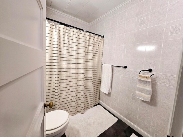 bathroom featuring tile walls, crown molding, a shower with shower curtain, and toilet