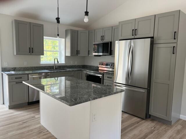 kitchen with lofted ceiling, sink, light wood-type flooring, stainless steel appliances, and a kitchen island