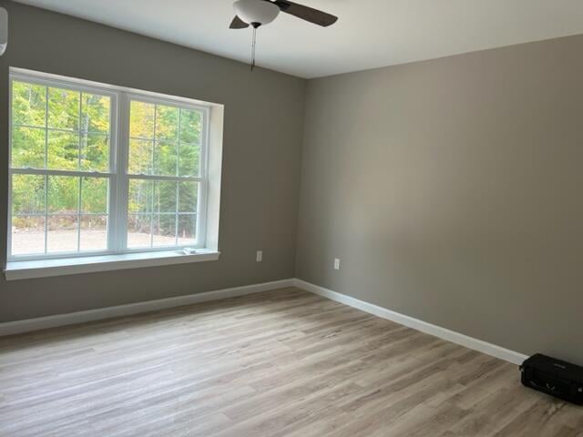 empty room featuring plenty of natural light, a wall mounted air conditioner, ceiling fan, and light wood-type flooring