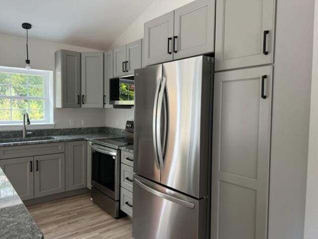 kitchen featuring appliances with stainless steel finishes, dark stone countertops, vaulted ceiling, sink, and light hardwood / wood-style flooring