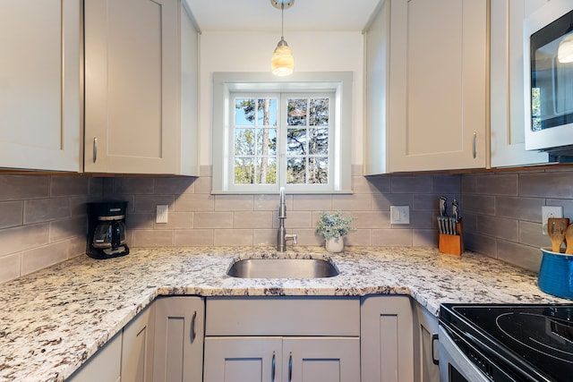 kitchen featuring light stone counters, sink, tasteful backsplash, gray cabinetry, and hanging light fixtures