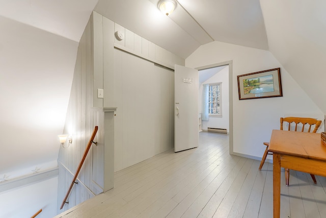 interior space featuring baseboard heating, light hardwood / wood-style floors, and vaulted ceiling