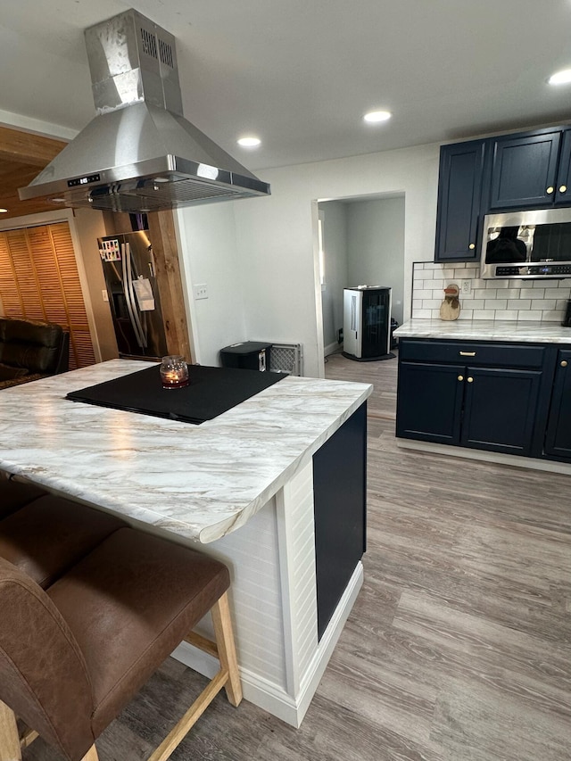 kitchen featuring backsplash, a kitchen breakfast bar, light hardwood / wood-style floors, stainless steel appliances, and island exhaust hood