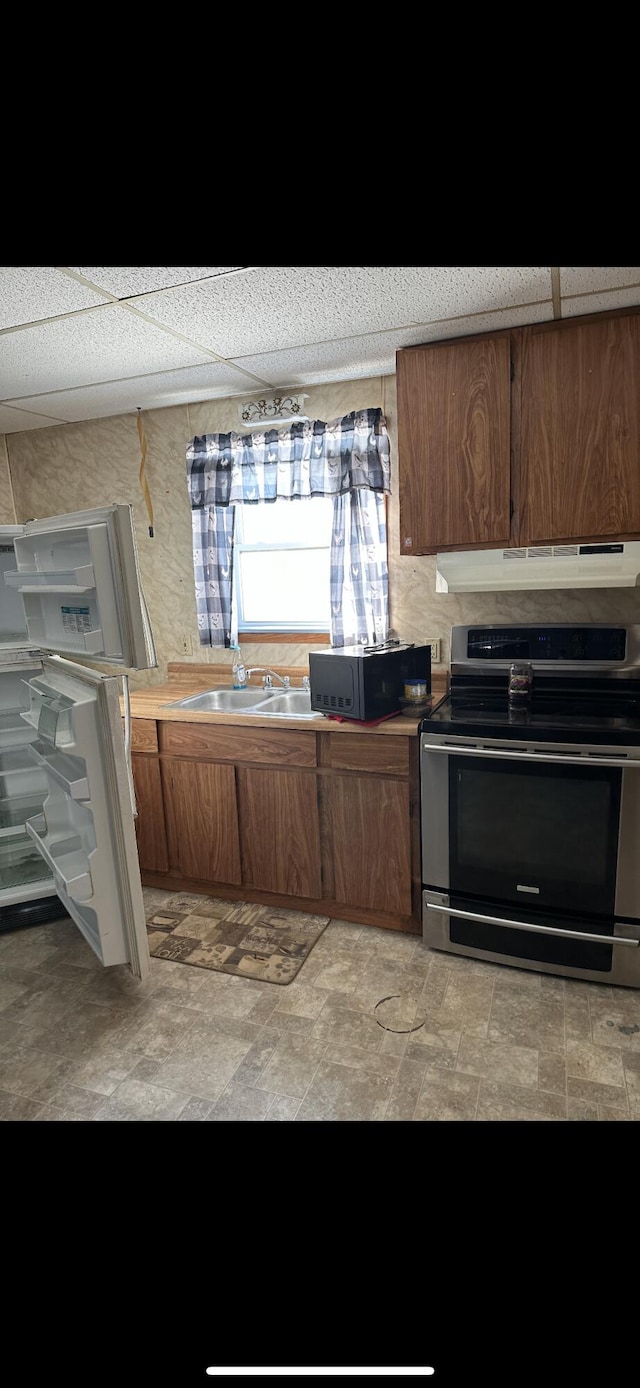 kitchen featuring a drop ceiling, white fridge, light tile floors, stainless steel electric range, and sink