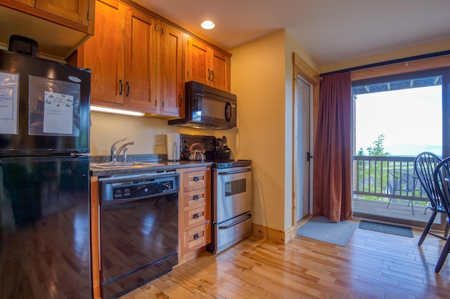 kitchen featuring brown cabinetry, a sink, black appliances, dark countertops, and light wood-type flooring