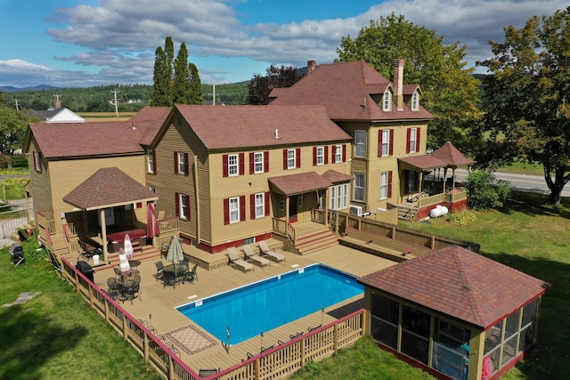 view of swimming pool with a deck, a lawn, a gazebo, and a sunroom