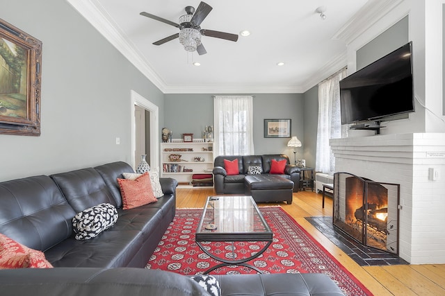 living room featuring a brick fireplace, ceiling fan, wood-type flooring, and ornamental molding