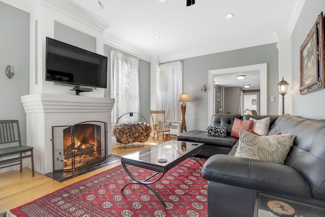 living room featuring hardwood / wood-style flooring, ornamental molding, decorative columns, and a fireplace