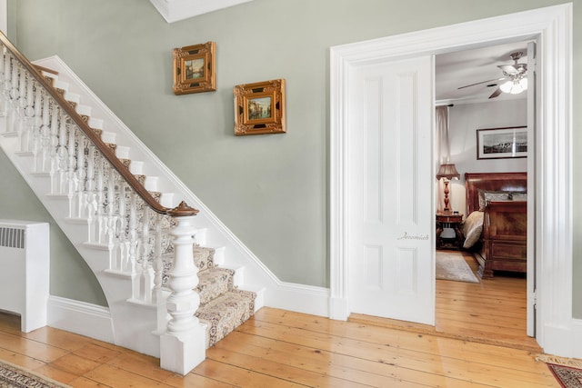 stairs featuring hardwood / wood-style flooring, ceiling fan, and radiator heating unit