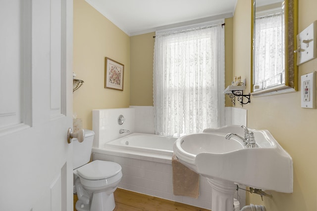 bathroom featuring hardwood / wood-style floors, ornamental molding, toilet, and a relaxing tiled tub