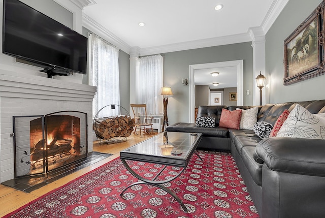 living room featuring hardwood / wood-style floors, crown molding, ornate columns, and a fireplace