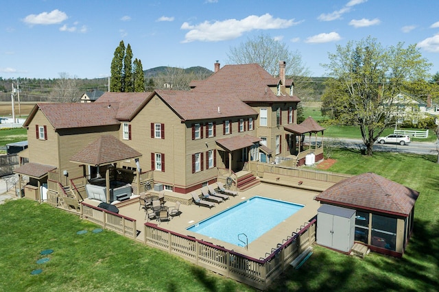 back of house featuring a lawn, a patio, a storage unit, and a swimming pool side deck