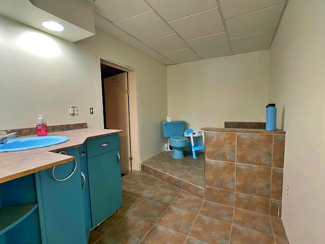 bathroom with tile flooring, a drop ceiling, toilet, and vanity