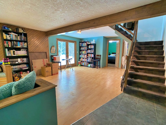 interior space with a textured ceiling, wood-type flooring, wood walls, and french doors