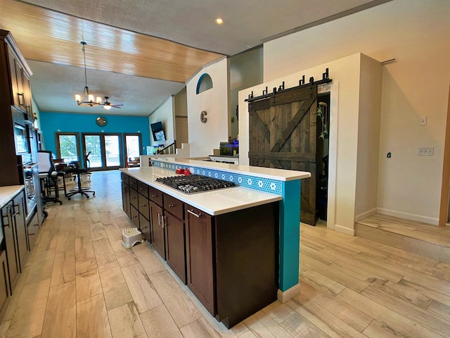kitchen with decorative light fixtures, dark brown cabinets, a barn door, and light hardwood / wood-style floors