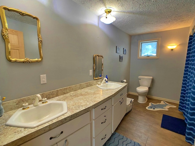 bathroom with a textured ceiling, dual vanity, and toilet