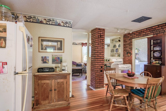 dining space with a textured ceiling, decorative columns, light hardwood / wood-style flooring, and brick wall