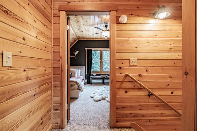 hall featuring carpet floors, wooden ceiling, wooden walls, and lofted ceiling