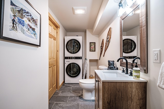 bathroom with stone finish flooring, vanity, toilet, and stacked washer / drying machine