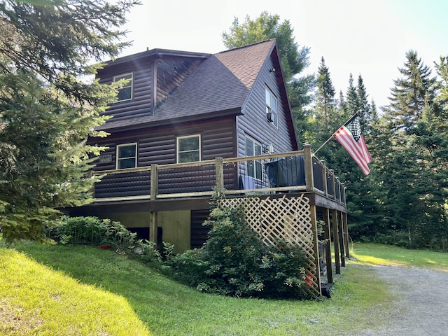 view of property exterior featuring a shingled roof, faux log siding, a yard, and a deck