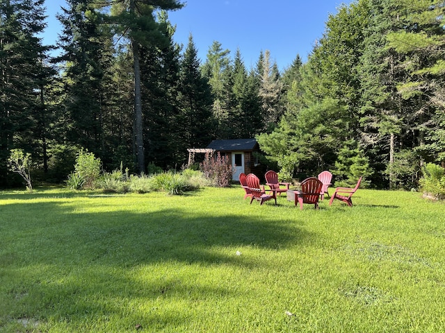 view of yard featuring an outbuilding, a wooded view, and a storage shed