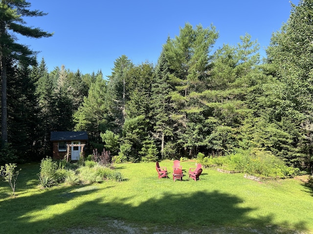 view of yard with a forest view, an outdoor structure, and a storage shed