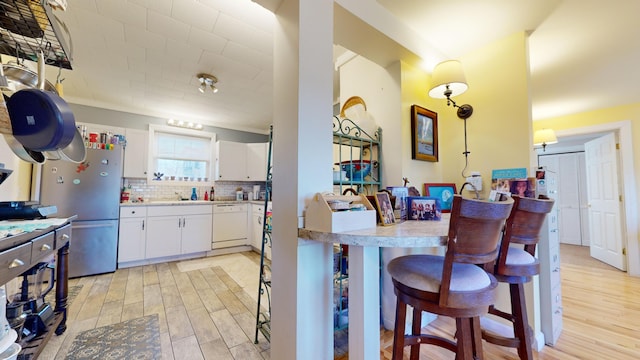 kitchen with white appliances, backsplash, a kitchen bar, white cabinetry, and light wood-type flooring