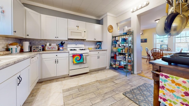 kitchen featuring backsplash, light tile flooring, white appliances, white cabinets, and crown molding