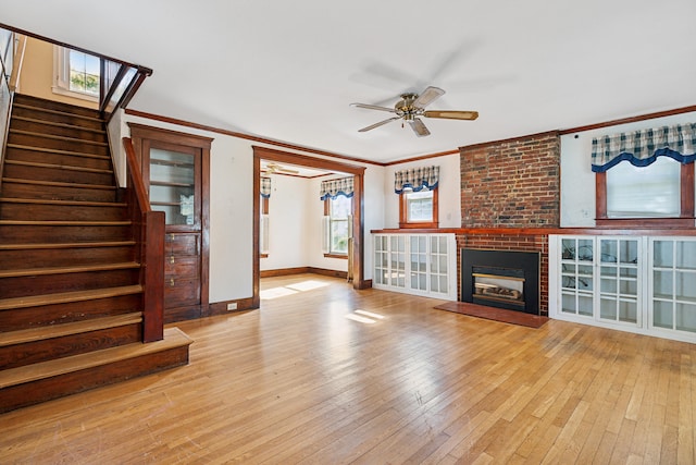 unfurnished living room featuring a brick fireplace, ornamental molding, light wood-type flooring, and ceiling fan