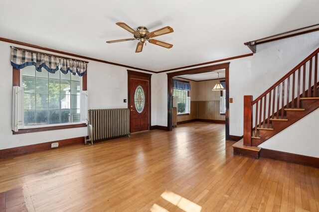 foyer entrance featuring ceiling fan, radiator, wood-type flooring, wooden walls, and ornamental molding