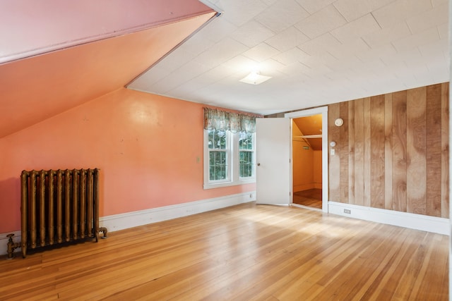 interior space featuring lofted ceiling, wood walls, hardwood / wood-style floors, and radiator heating unit