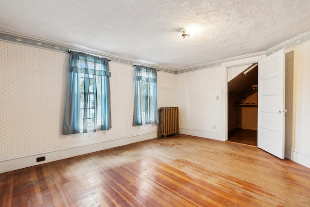 spare room featuring radiator heating unit, hardwood / wood-style flooring, and a textured ceiling