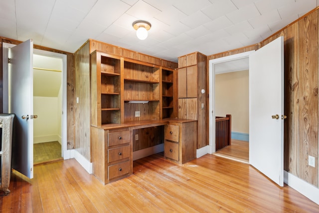 unfurnished office featuring built in shelves, light hardwood / wood-style flooring, and wooden walls