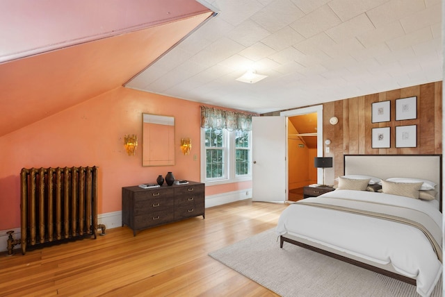 bedroom featuring lofted ceiling, radiator heating unit, a walk in closet, a closet, and light hardwood / wood-style floors