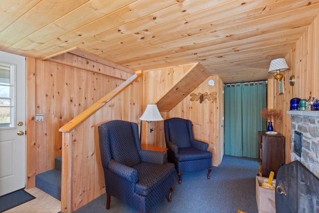 sitting room featuring light carpet, wooden ceiling, wood walls, and a stone fireplace