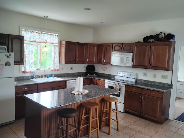 kitchen with light tile patterned floors, a breakfast bar area, white appliances, a kitchen island, and sink