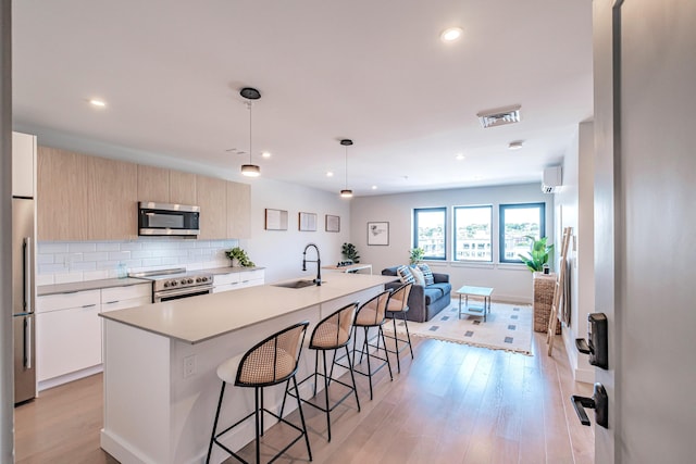 kitchen with appliances with stainless steel finishes, backsplash, sink, hanging light fixtures, and an island with sink